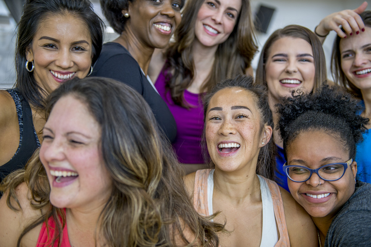 Un groupe multiethnique de femmes adultes pose ensemble. Elles se trouvent dans un centre de santé et portent des vêtements de sport. Les amies sourient et rient ensemble.